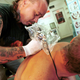 Tattoo artist leaning over to tattoo man's back